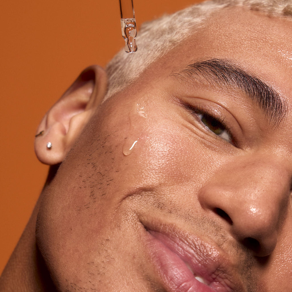 Close-up of a man's face with a droplet of Vitamin C serum on his cheek